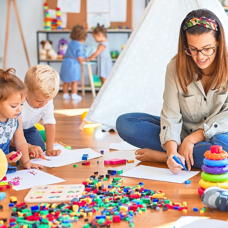 Eine Frau sitzt auf dem Boden, während ihre Kinder um sie herum spielen und eine fröhliche Atmosphäre schaffen.
